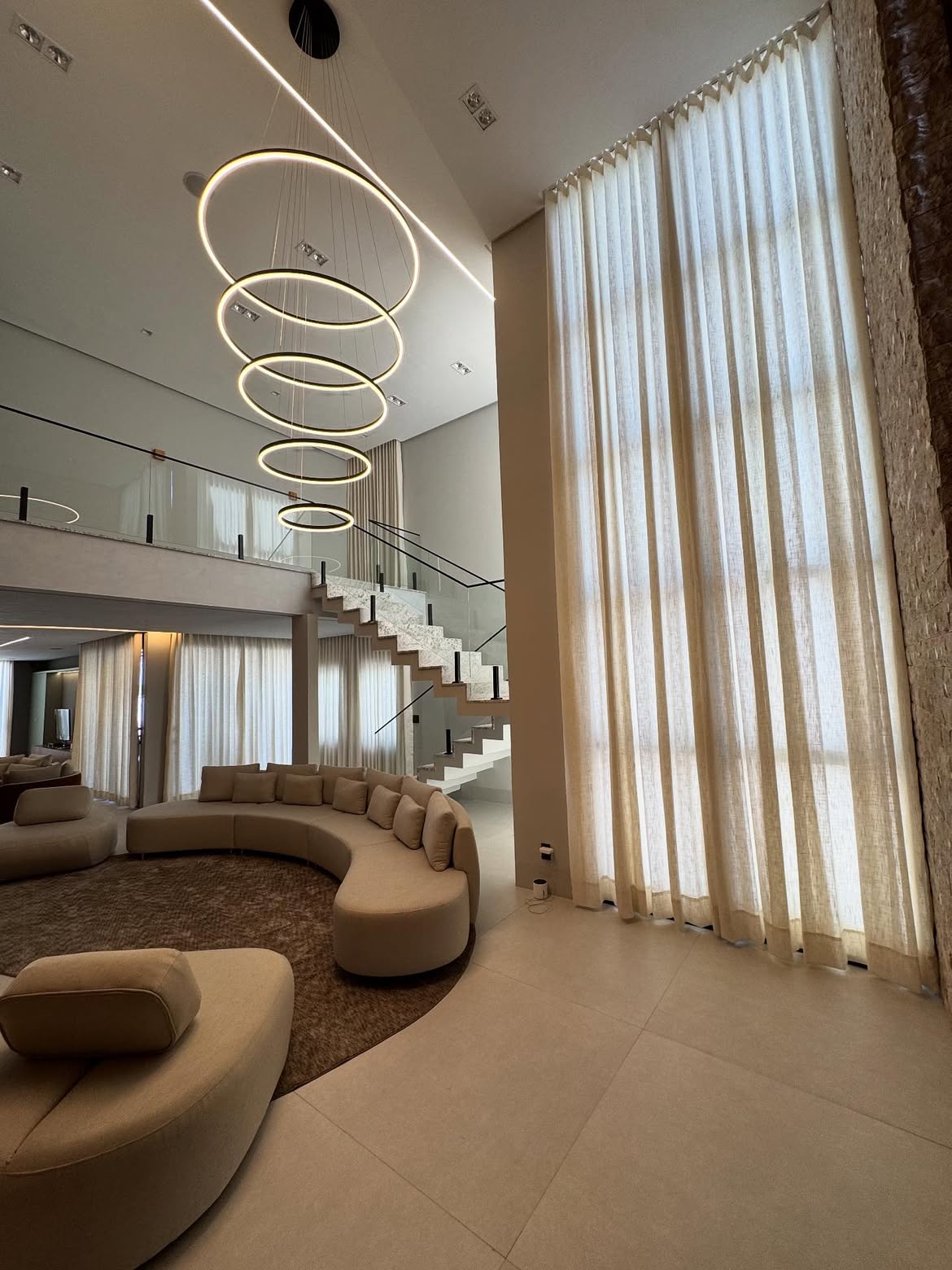 Living de pé-direito duplo com cortinas sob medida e luz natural filtrada por tecido